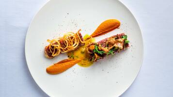 A white plate with a dish consisting of a meat fillet, vegetables, and a sauce.