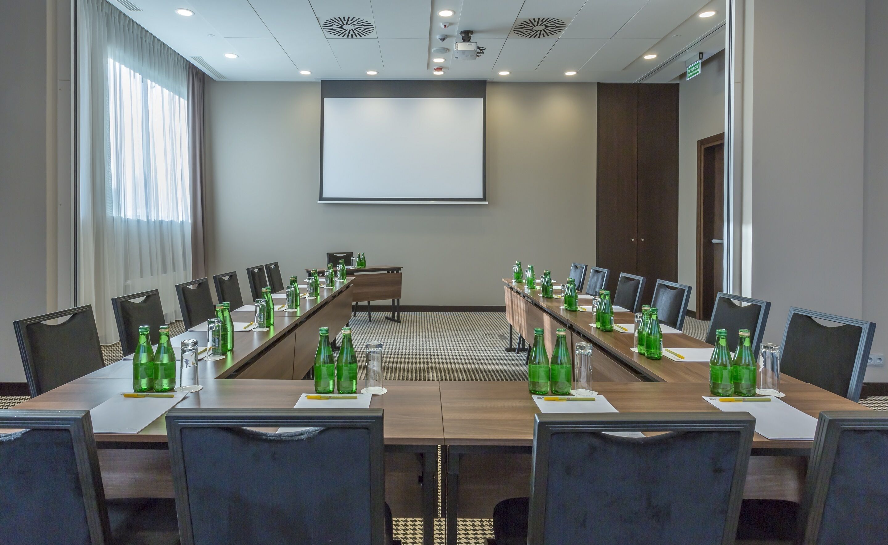 Un salón de conferencias con una larga mesa, sillas y una pantalla de proyector.