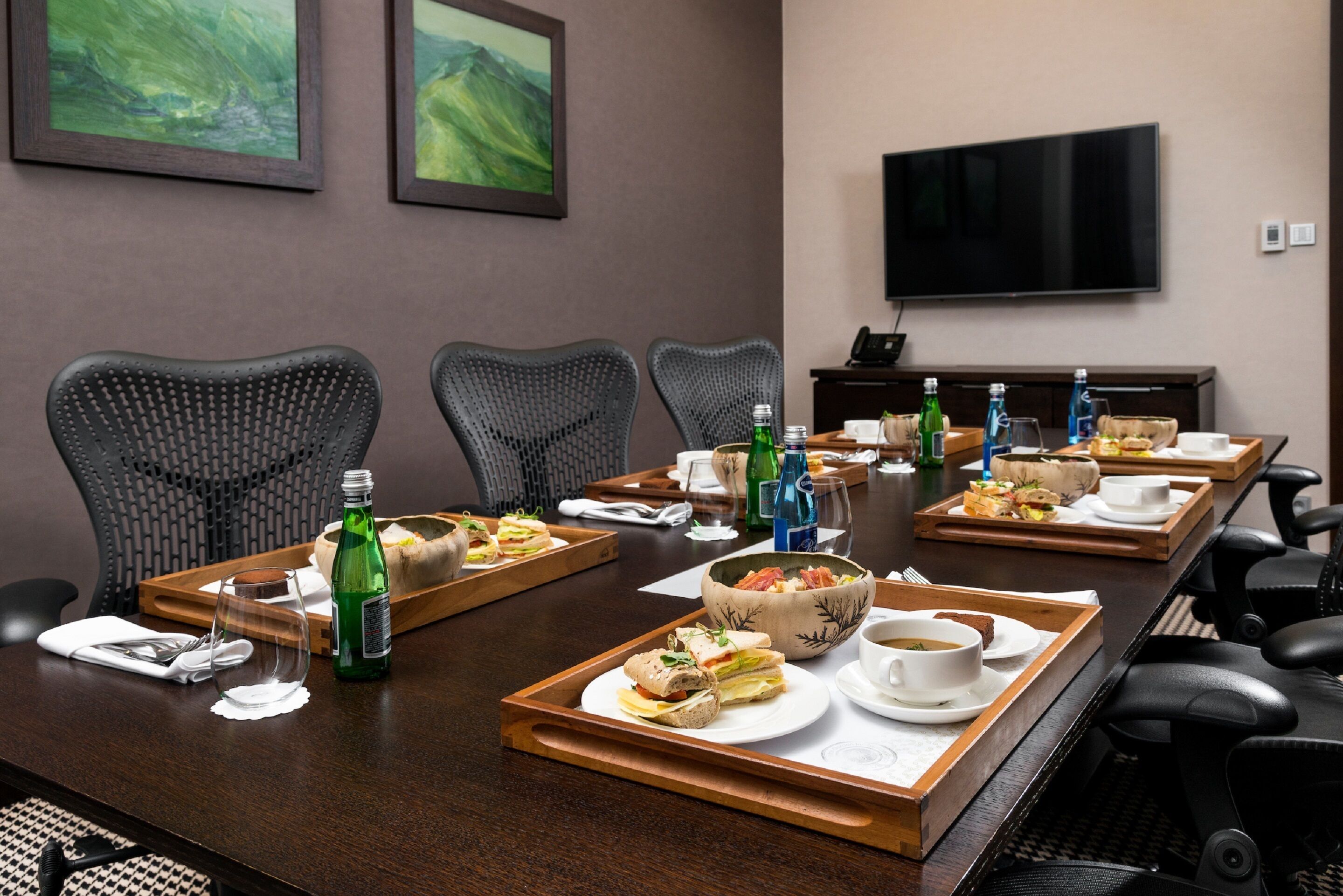 A conference room with a long table set for a meeting, equipped with chairs, trays of food, and beverages.