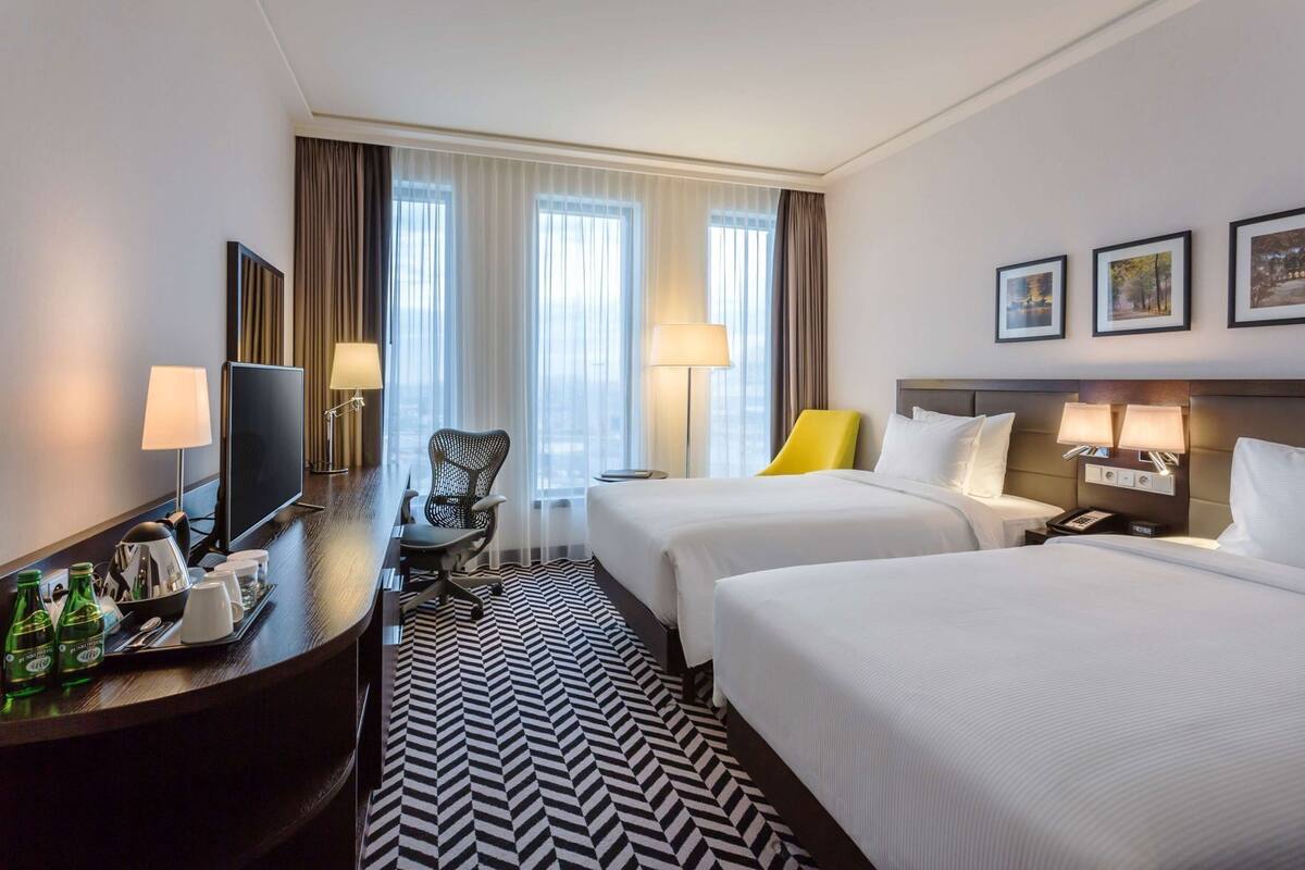 Une chambre d’hôtel avec deux lits, un bureau avec une télévision, une chaise et une lampe.