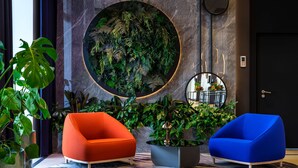 A modern lobby with a large circular wall art, two vibrant armchairs, and various potted plants.
