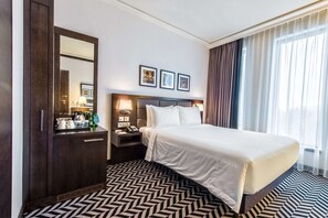 A hotel room with a large bed, a dresser, a nightstand, a mirror, and a window with curtains.