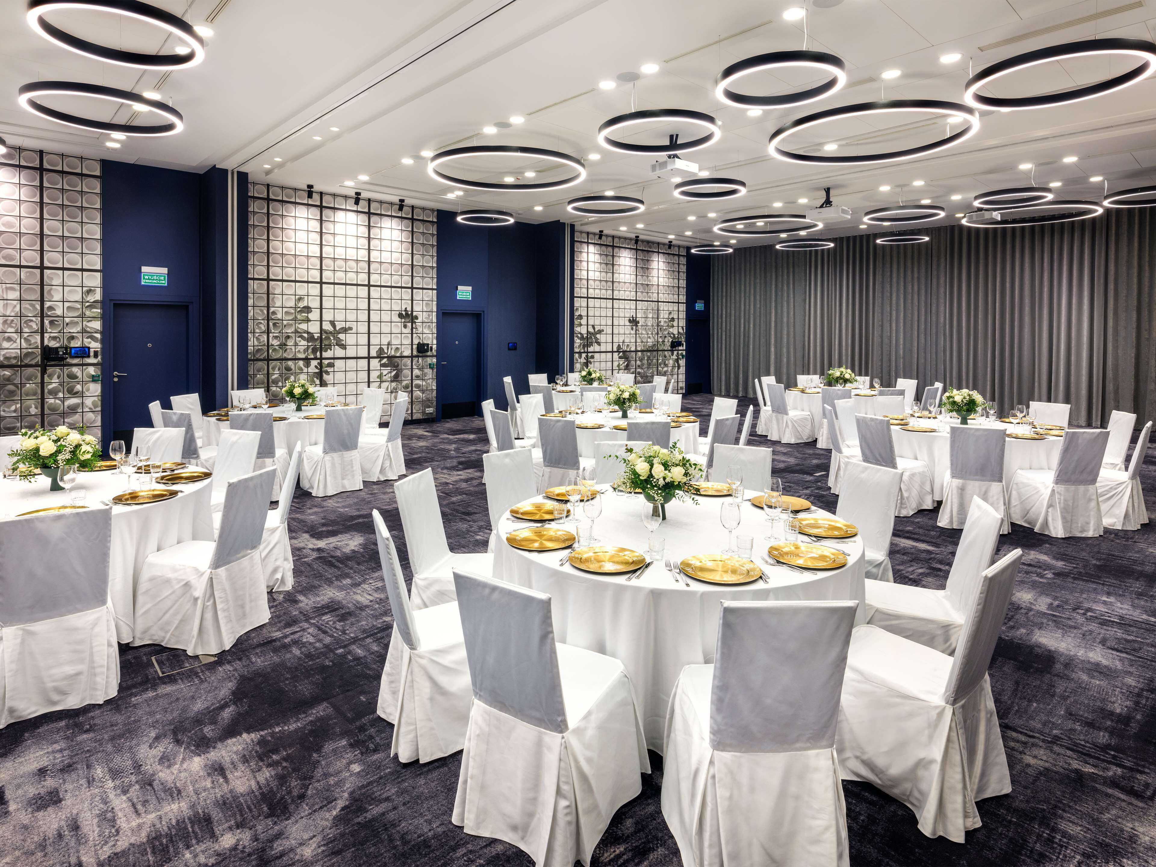 Une salle de banquet avec des tables rondes, des nappes blanches et des chaises grises.