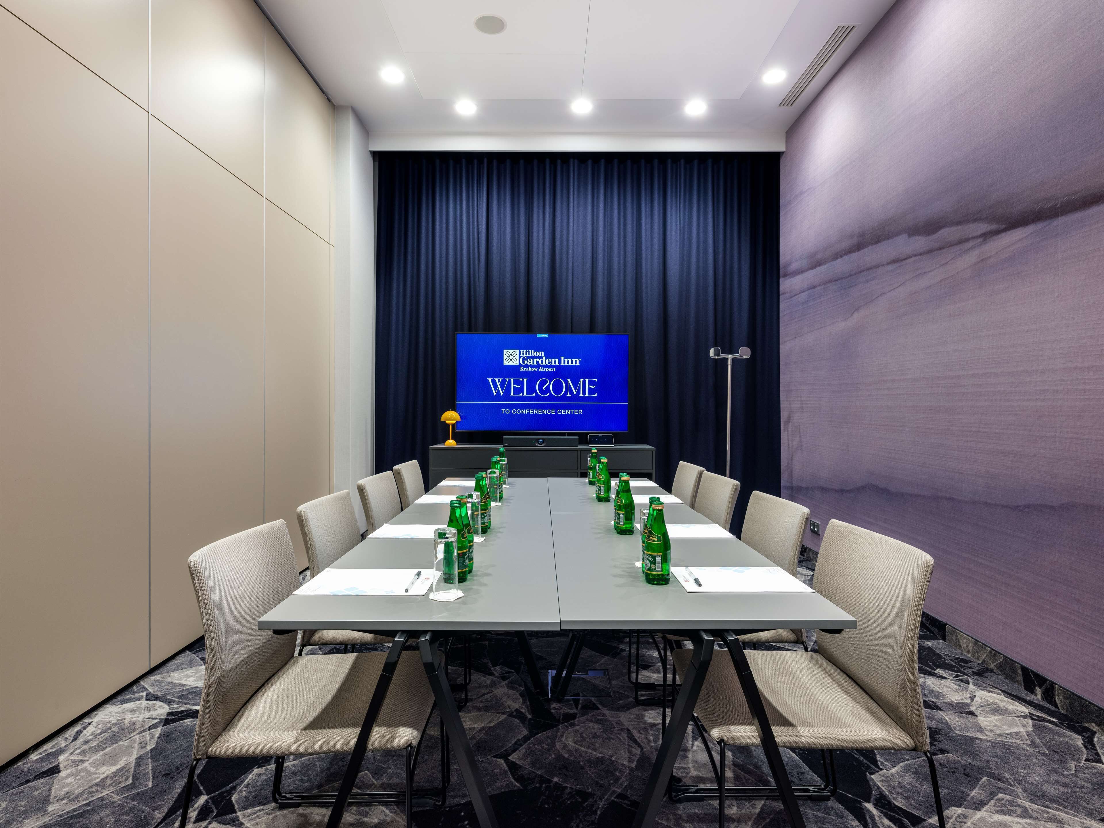 A conference room with a long table, chairs, a screen displaying 'Hilton Garden Inn', and a carpeted floor.