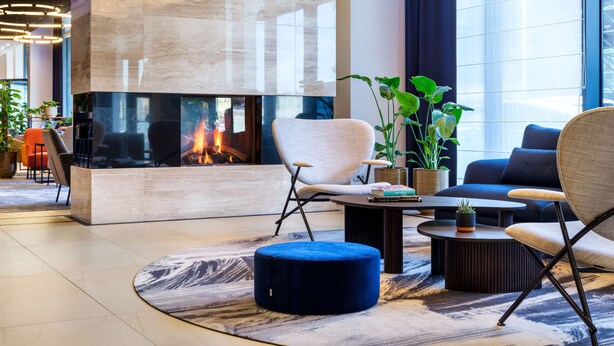 A modern lounge area with a stone fireplace, comfortable seating, and large windows.