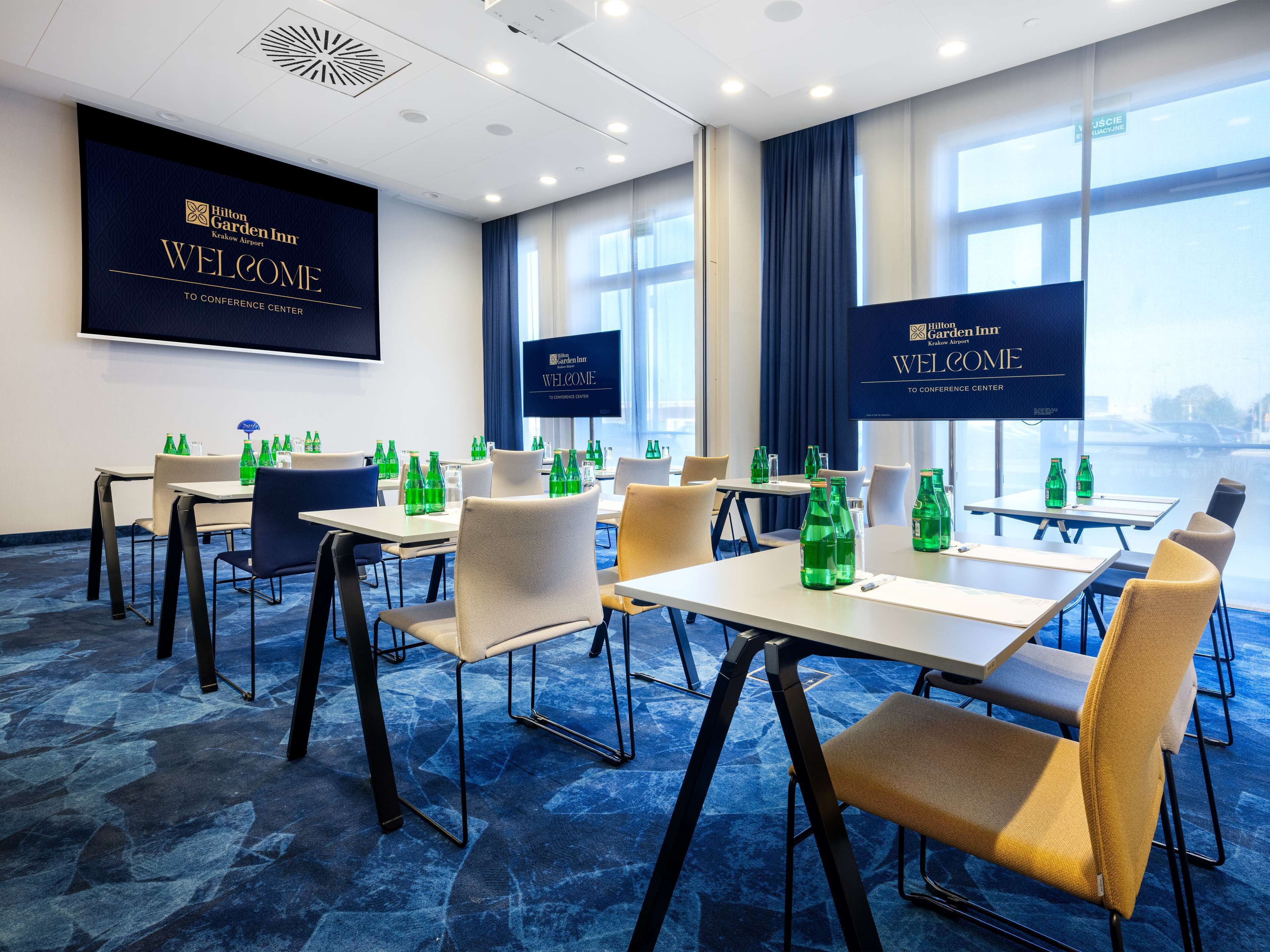 A conference room with tables and chairs, large windows, and a 'Welcome' sign.
