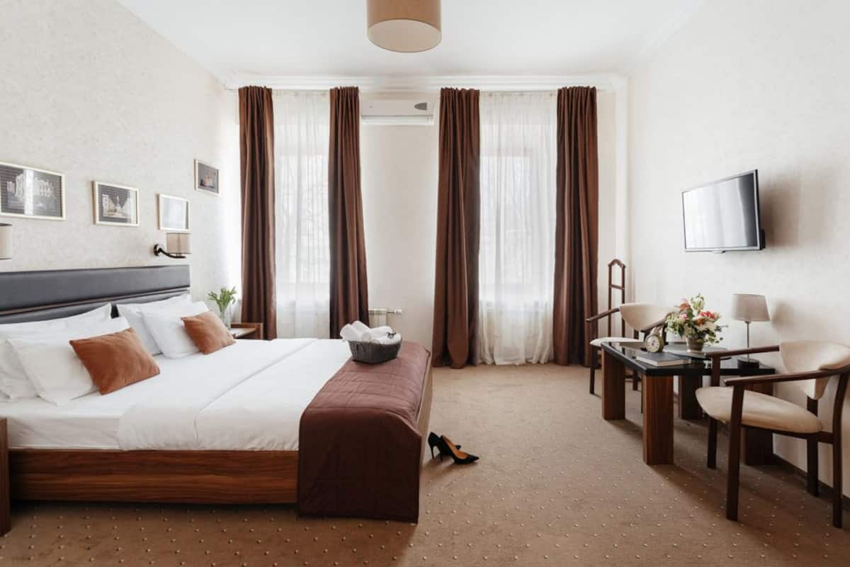Habitación de hotel con cama, escritorio con silla, televisión y ventana con cortinas.