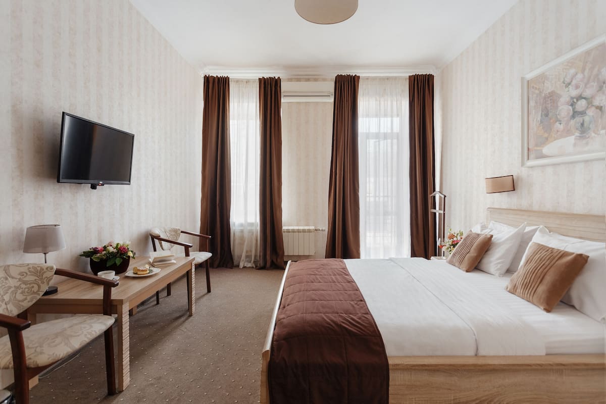 Una habitación de hotel con cama, escritorio, silla, televisor y cortinas.