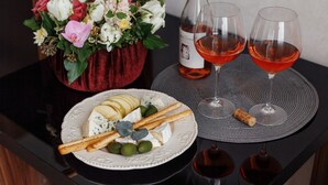 A table with a plate of cheese, crackers, and olives, two glasses of red wine, a bottle of wine, and a flower arrangement. - Ribas (Odesa)