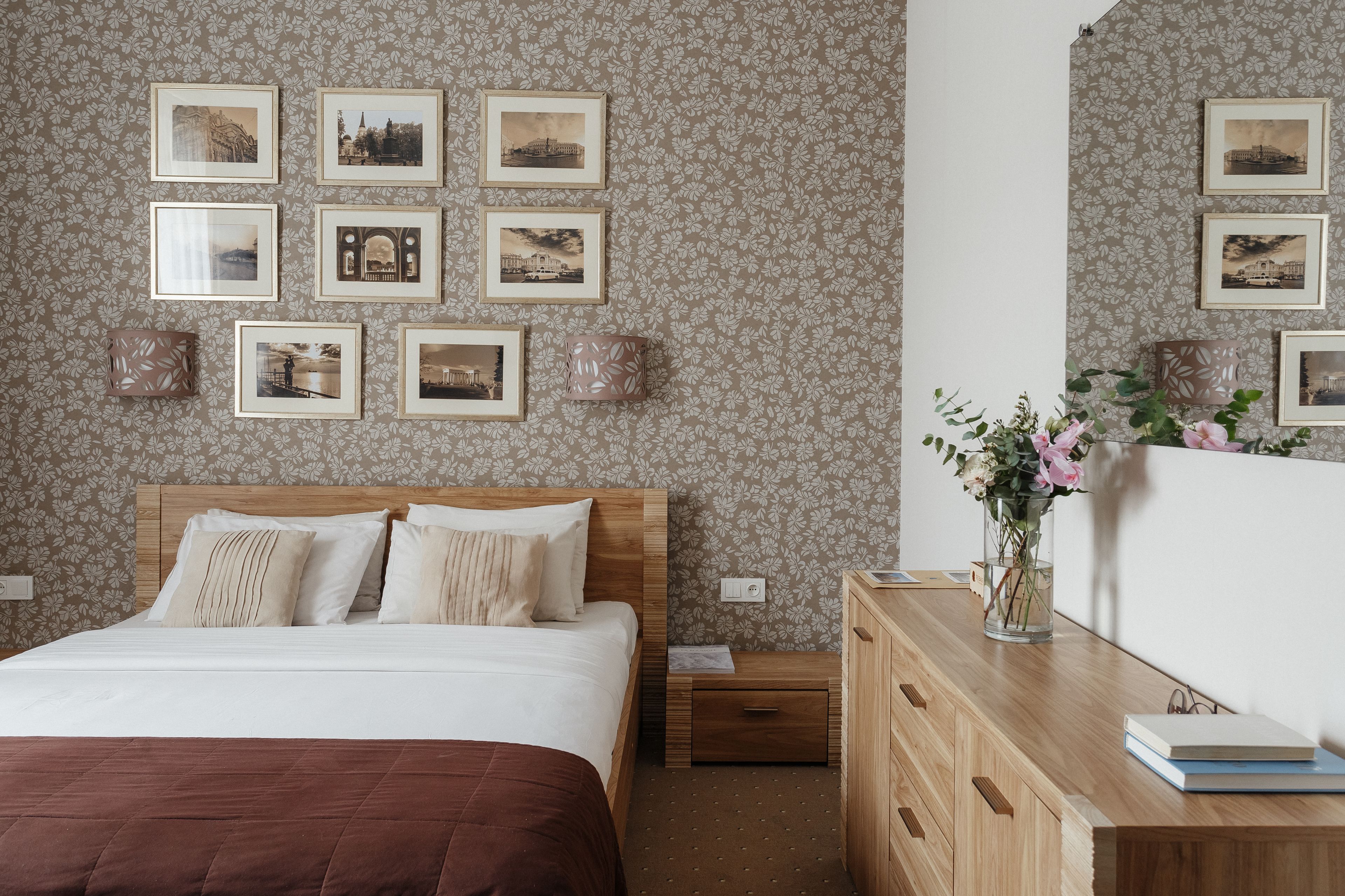 A neatly arranged bedroom with a wooden bed, a nightstand, a dresser, and a wall adorned with framed pictures.