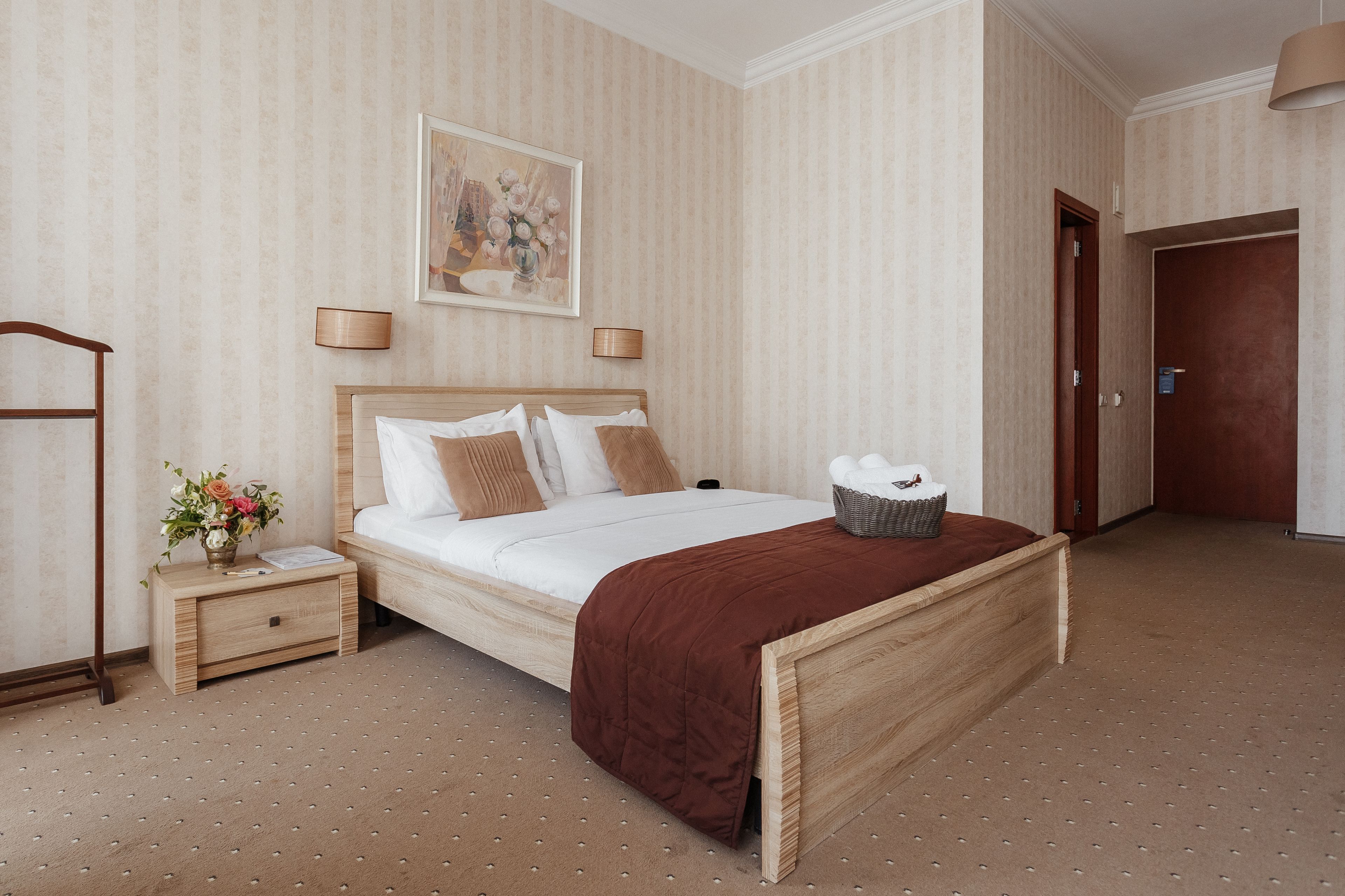 Une chambre à coucher bien rangée, avec un lit en bois, une table de chevet ornée d’un vase de fleurs et une porte donnant sur une autre pièce.
