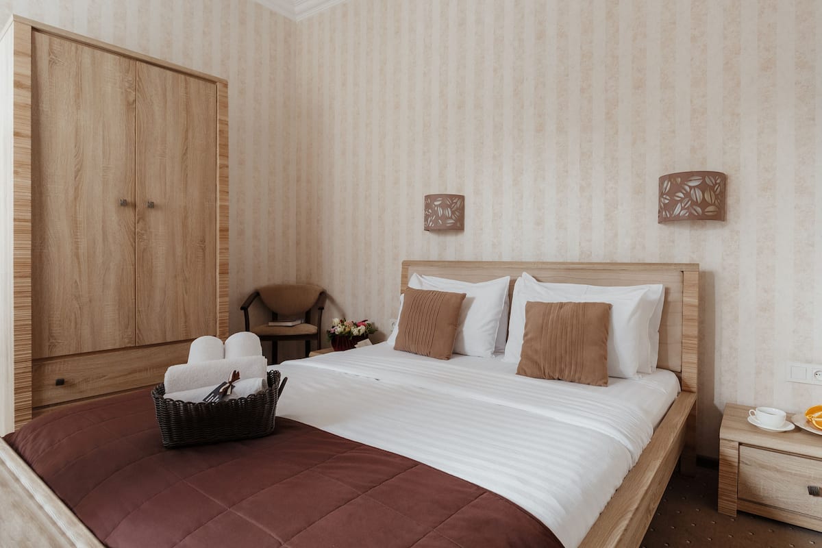 Habitación de hotel con un armario grande, una cama con sábanas blancas, un cabecero marrón y una mesita de noche con una taza y un platillo.