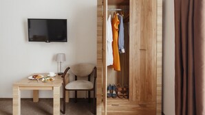 A room with a wooden wardrobe, a TV mounted on the wall, a dining table with plates and a chair, and a pair of shoes in the wardrobe. - Ribas (Odesa)