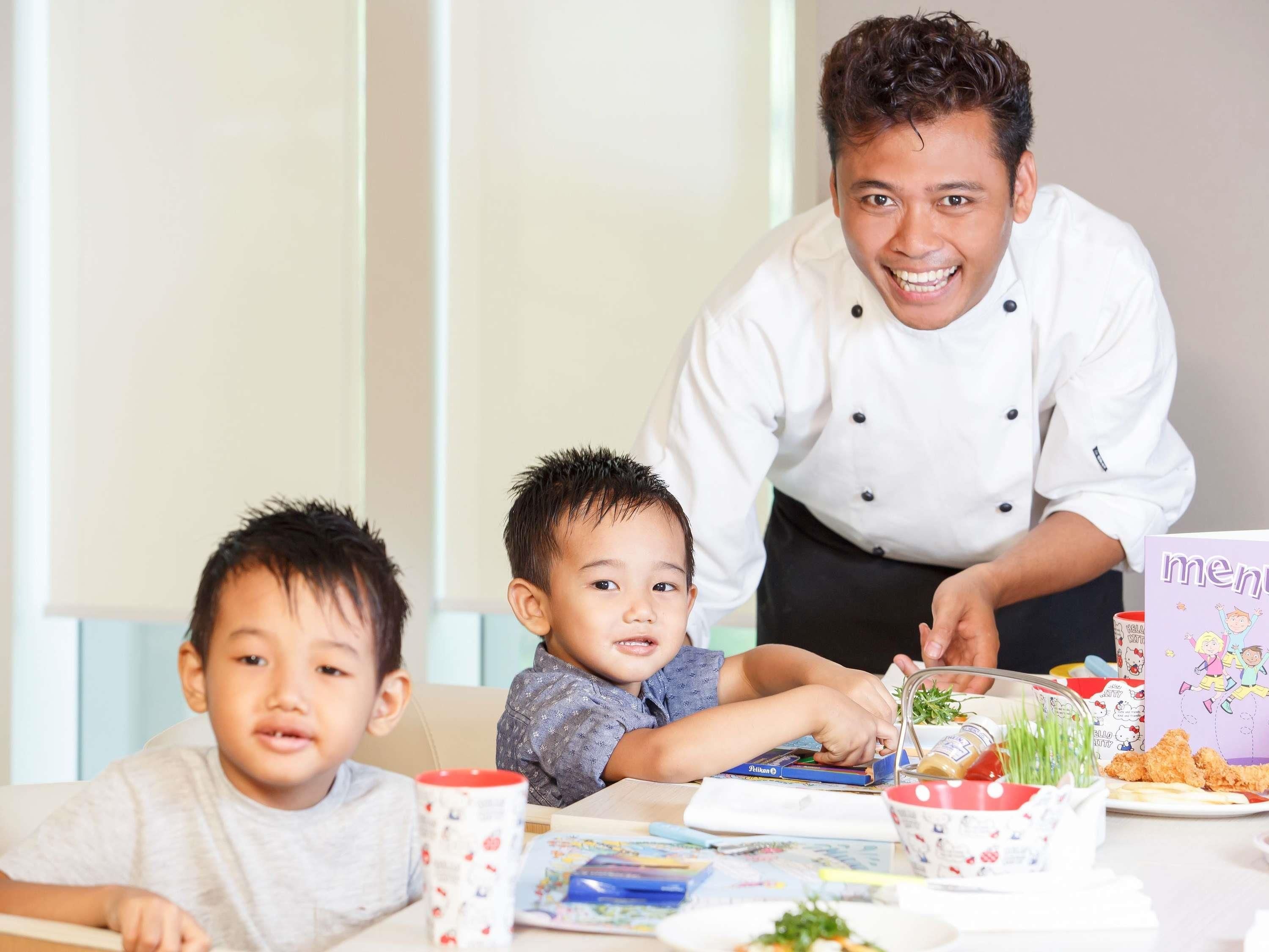 A dining table with a chef, two children, and a menu.
