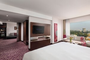 Habitación de hotel con una cama grande, un televisor montado en la pared, un sofá y vistas a la ciudad.