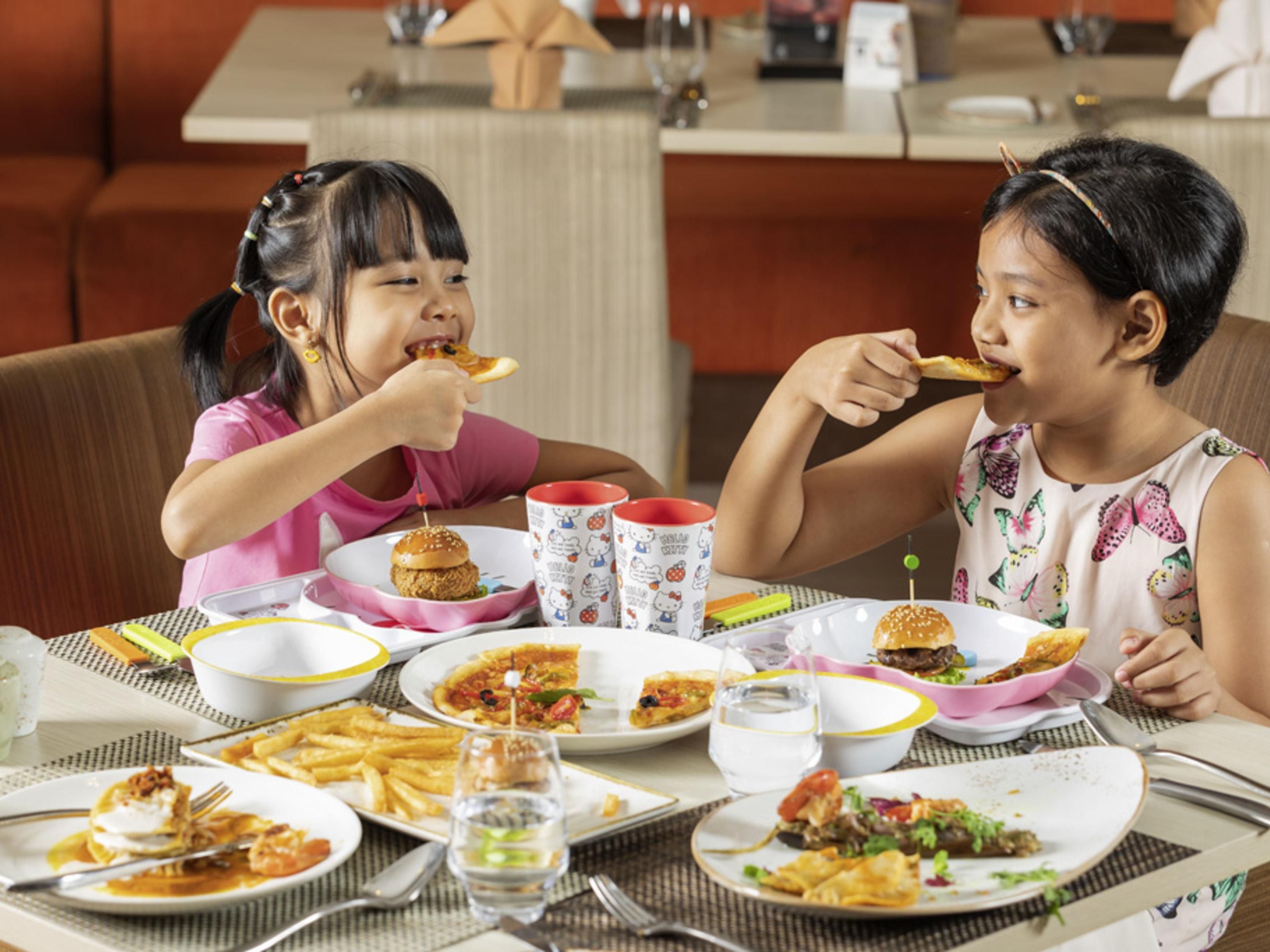 A dining table with various dishes, including burgers and fries, and a Hello Kitty mug.