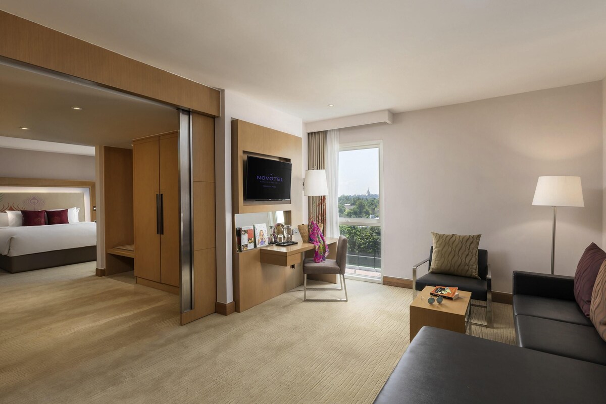 Habitación de hotel con cama, escritorio con televisor, sofá y balcón con vistas.