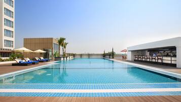 Relax by the pool surrounded by lounge chairs and umbrellas, with a bar nearby.