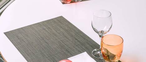 A round table with two wine glasses and a red tumbler on a white tablecloth.