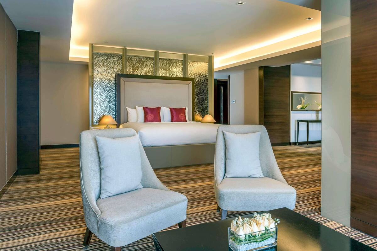 A hotel room with a large bed, two armchairs, a coffee table, and a small table with flowers.