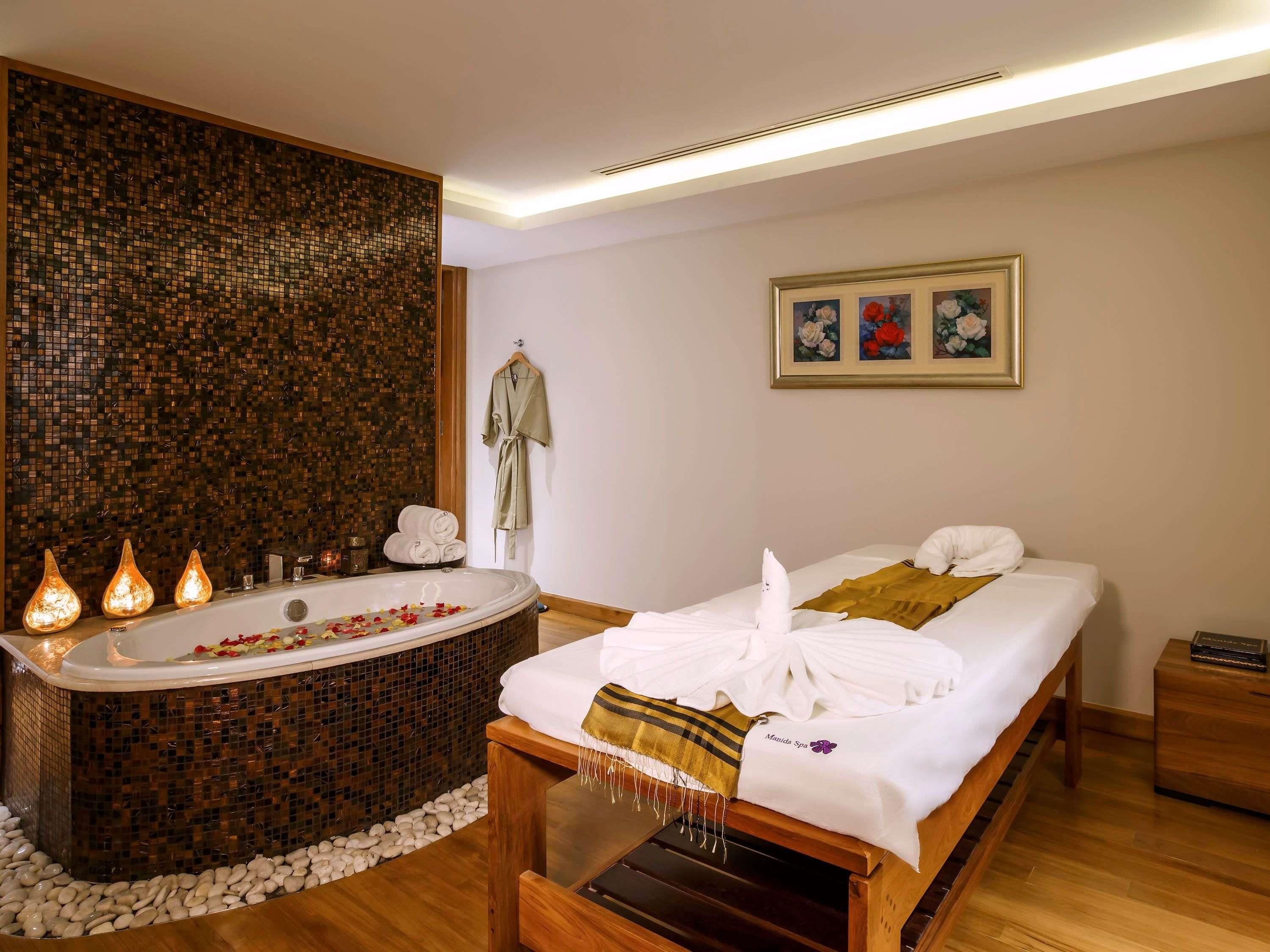 A spa room with a large bathtub, a wooden bench, and a bed with towels.