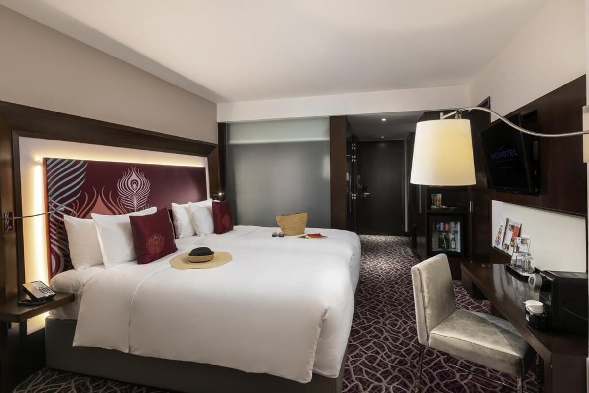 A hotel room with a large bed, a desk with a lamp, a chair, and a minibar.