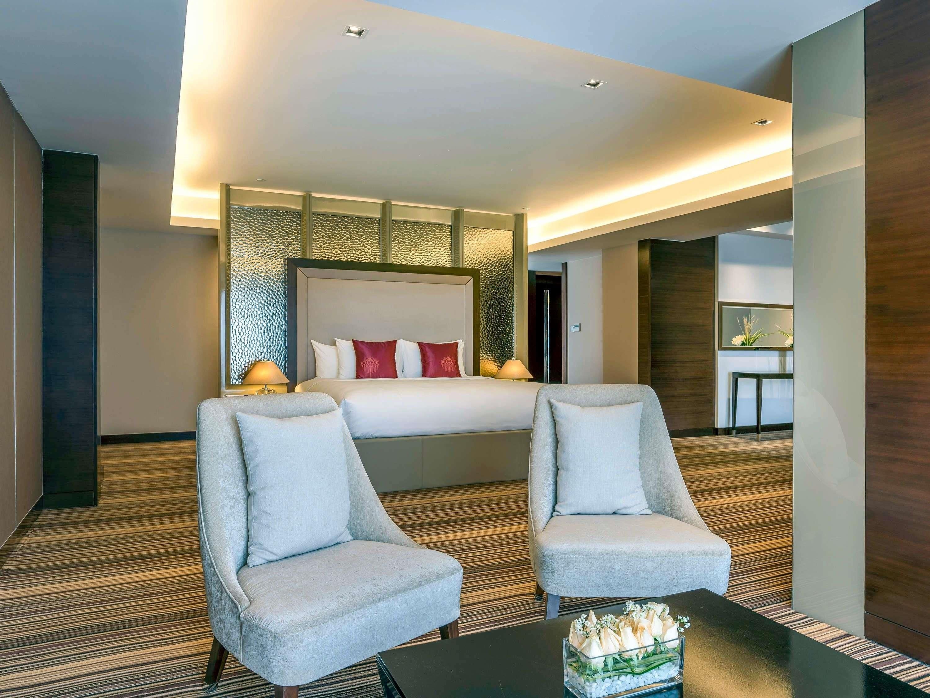A hotel room with a large bed, two armchairs, a coffee table, and a small table with flowers.