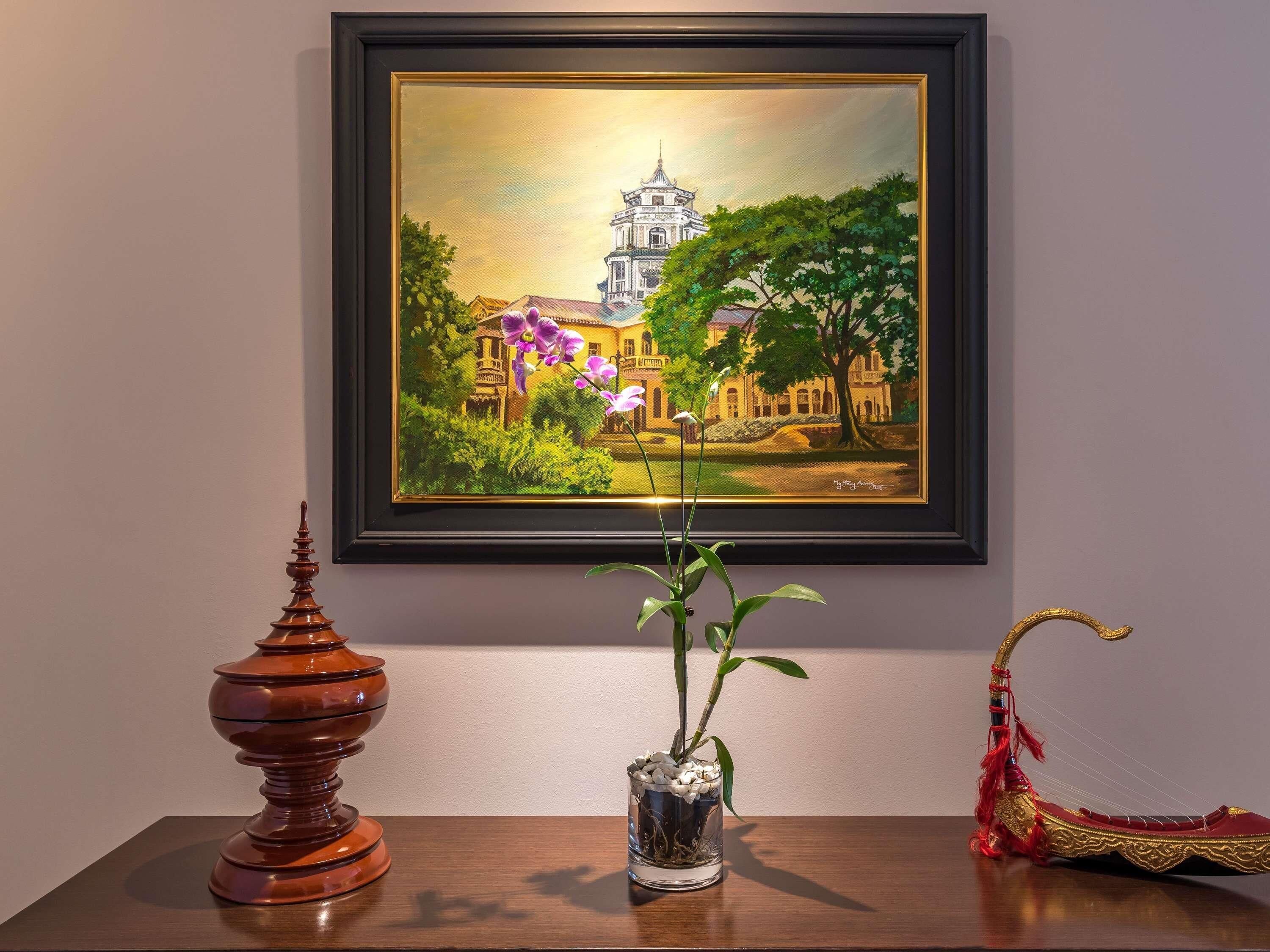 A framed painting of a traditional building with a tower, a vase with a plant, and a decorative object on a table.
