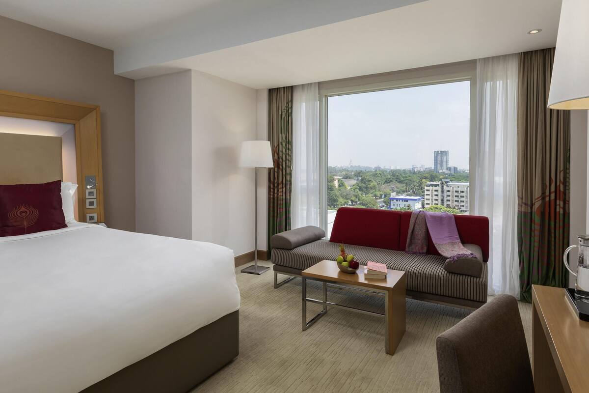 A hotel room with a bed, a sofa, a coffee table, and a view of the city.