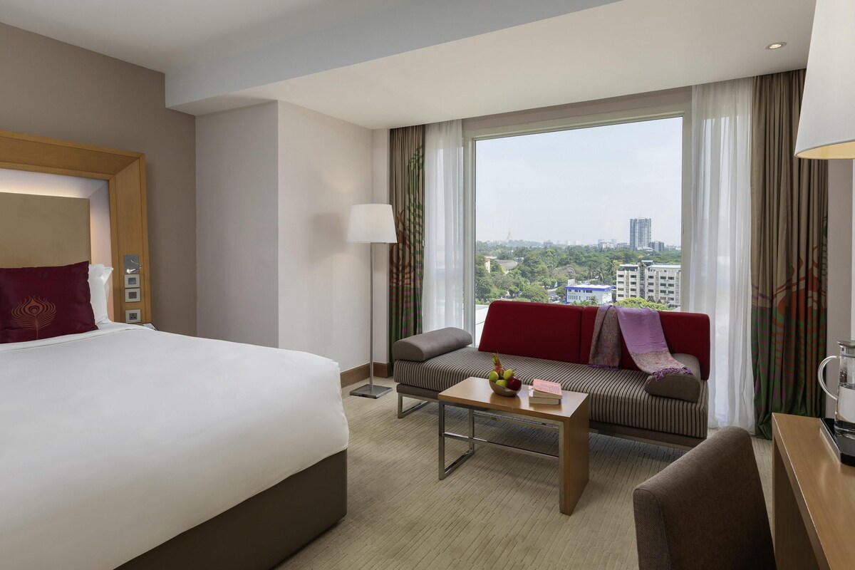 A hotel room with a bed, a sofa, a coffee table, and a view of the city.