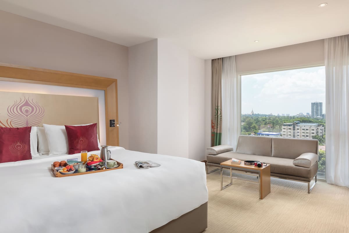 A hotel room with a large bed, a sofa, a coffee table, and a view of the city through the window.