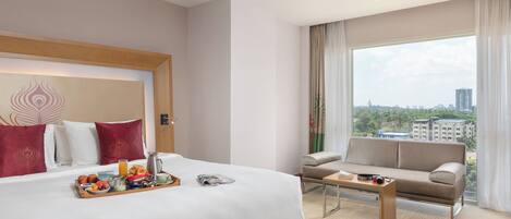 Habitación de hotel con una cama grande, un sofá, una mesa de centro y vista a la ciudad desde la ventana.