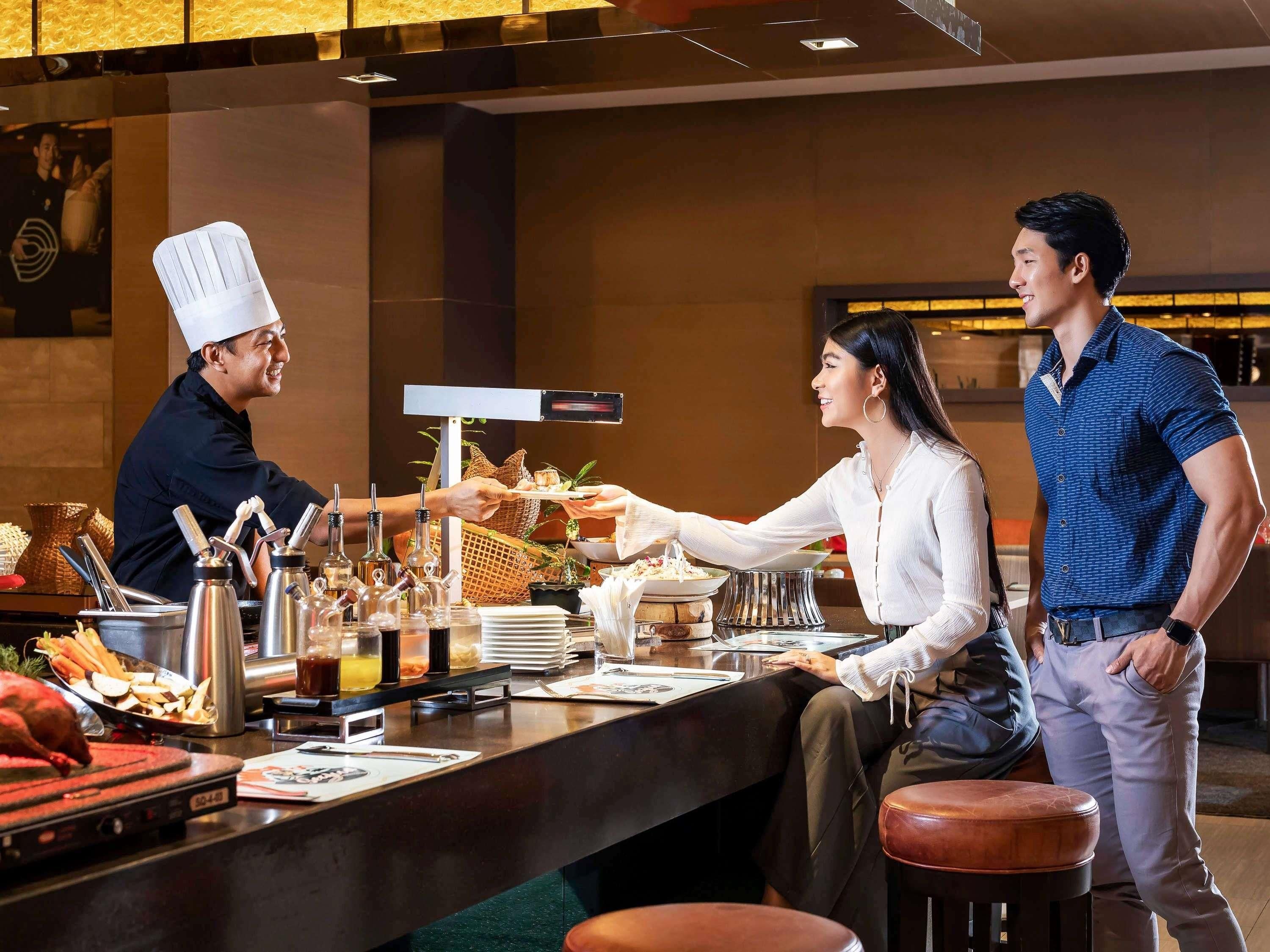 Una barra de restaurante con un chef sirviendo comida a un cliente y un camarero.