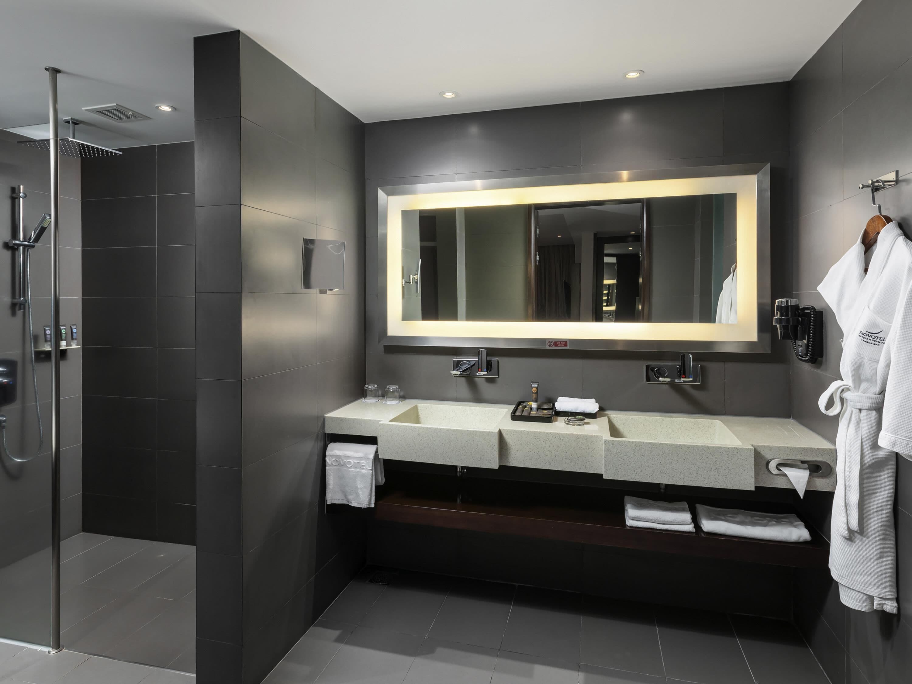 Une salle de bain moderne avec un grand miroir, deux vasques, une douche et un peignoir accroché au mur.