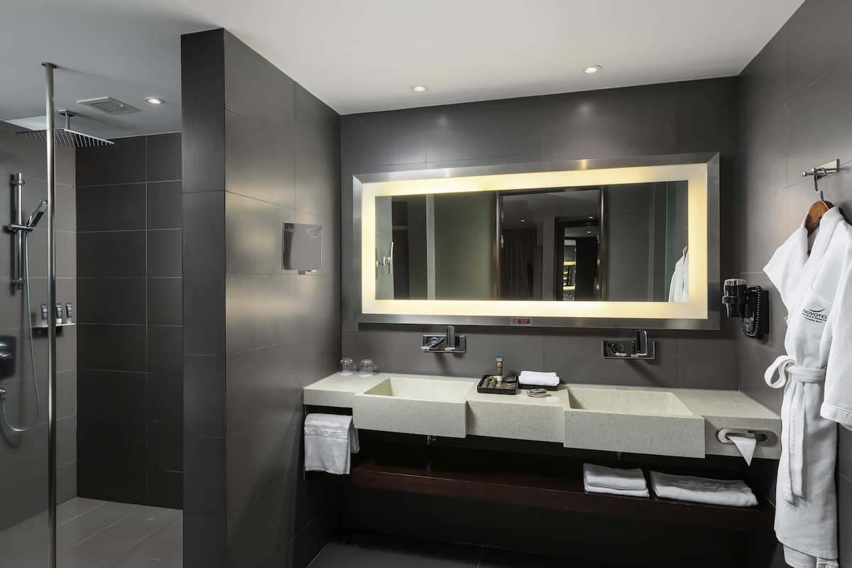 Une salle de bain moderne avec un grand miroir, deux vasques, une douche et un peignoir accroché au mur.