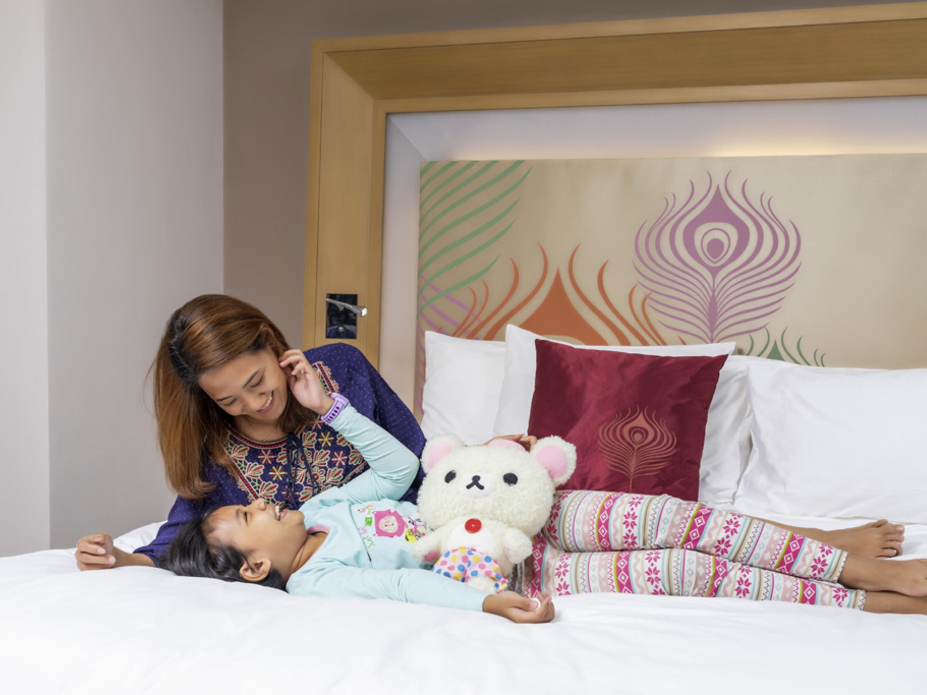 Un niño y un adulto descansan sobre una cama con un cabecero decorativo, almohadas y un peluche.
