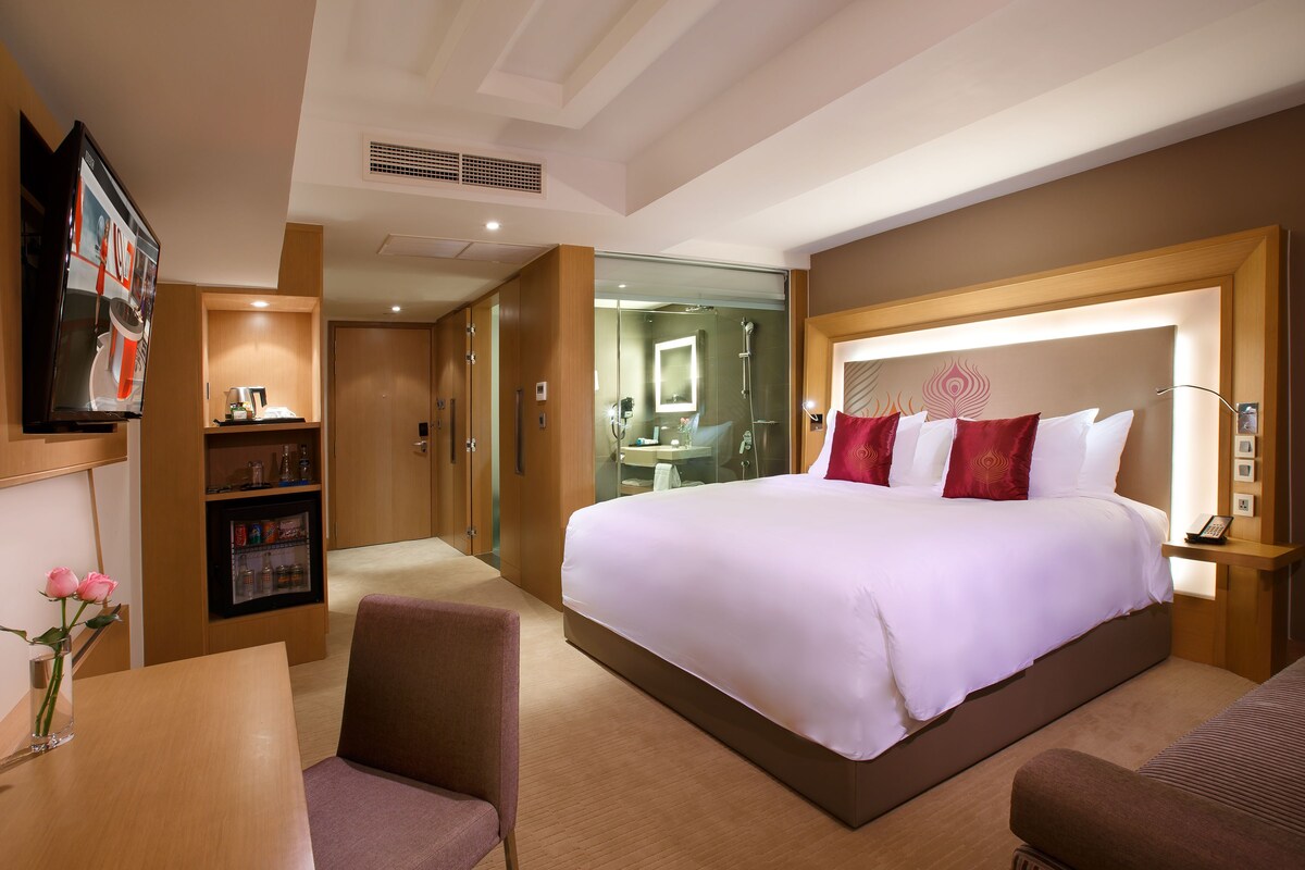 A hotel room with a large bed, a desk, a chair, a TV, and a minibar.