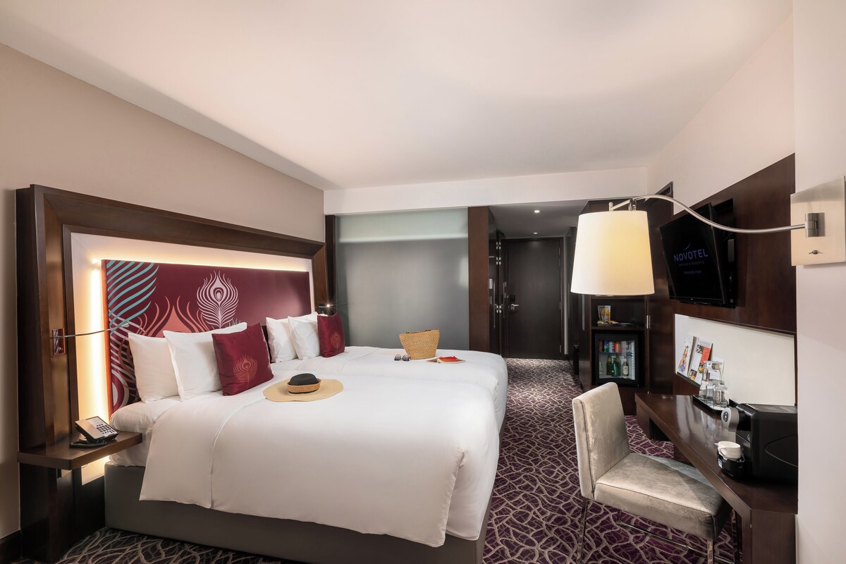 A hotel room with a large bed, a desk, a television, and a minibar.