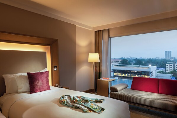 Habitación de hotel con cama, sofá rojo, lámpara y vistas a la ciudad.