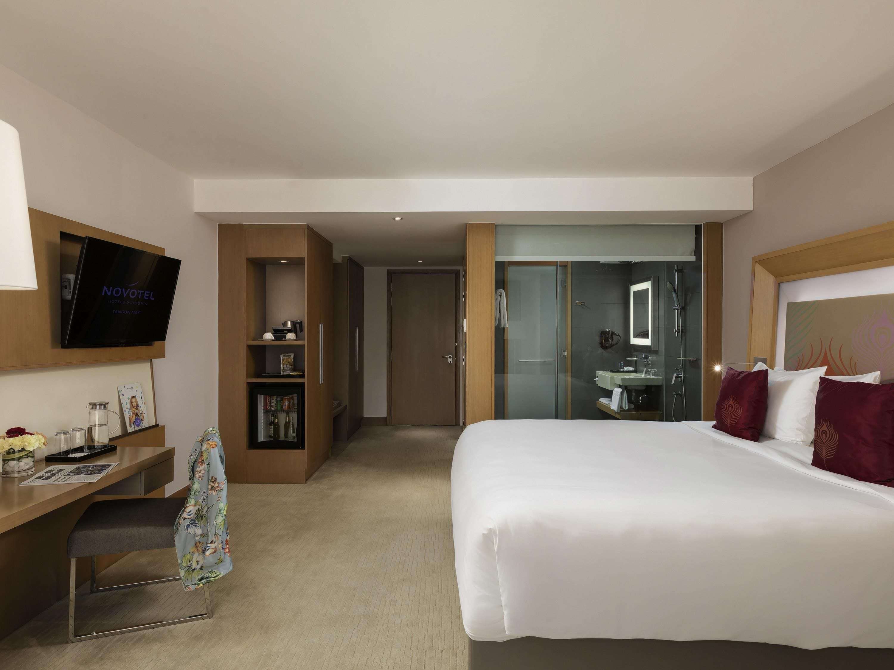 A hotel room with a bed, a TV, a desk, a bookshelf, and a bathroom visible through an open door.
