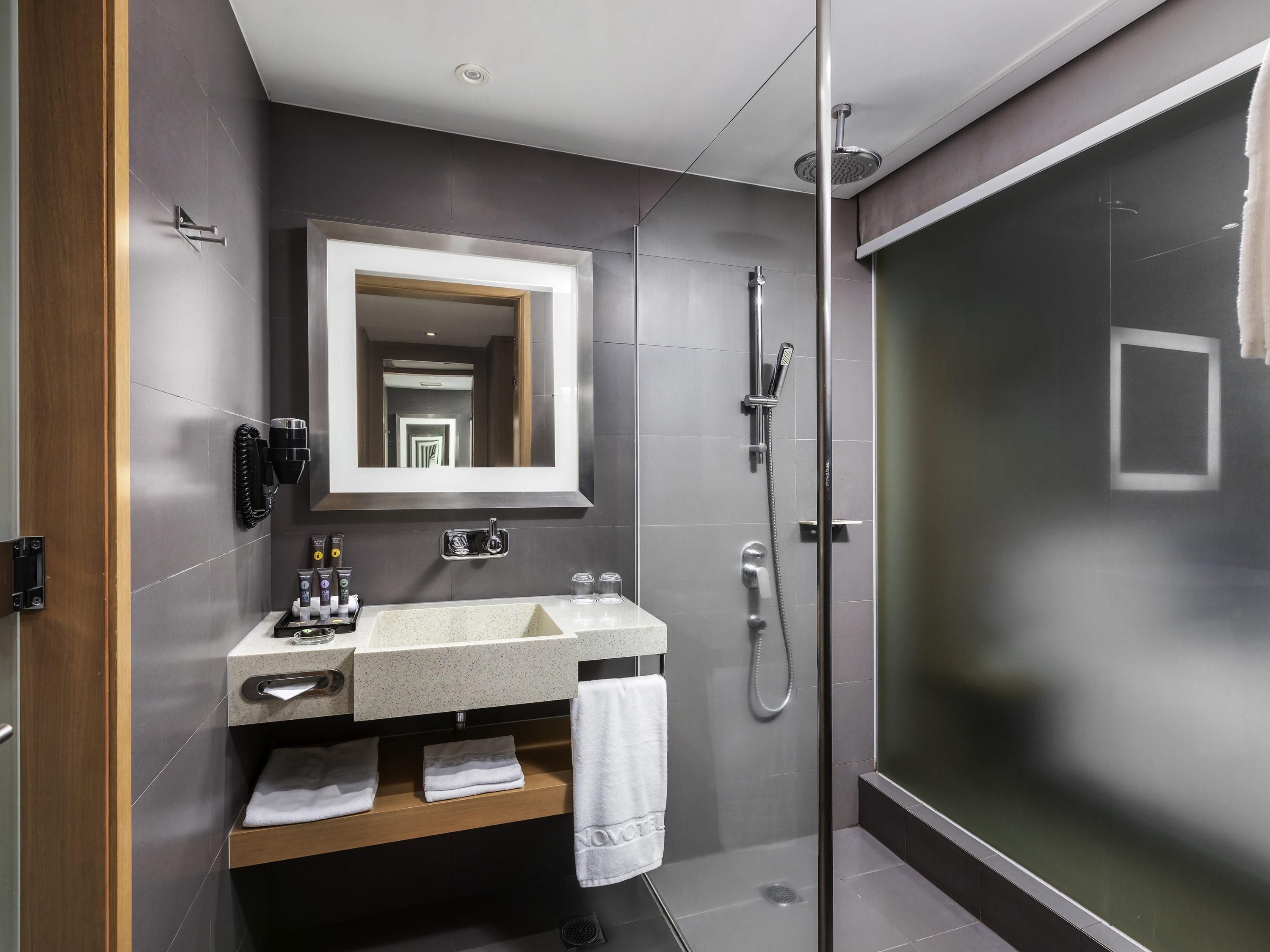 A modern bathroom with a glass shower enclosure, a large mirror, and a vanity with a towel rack.