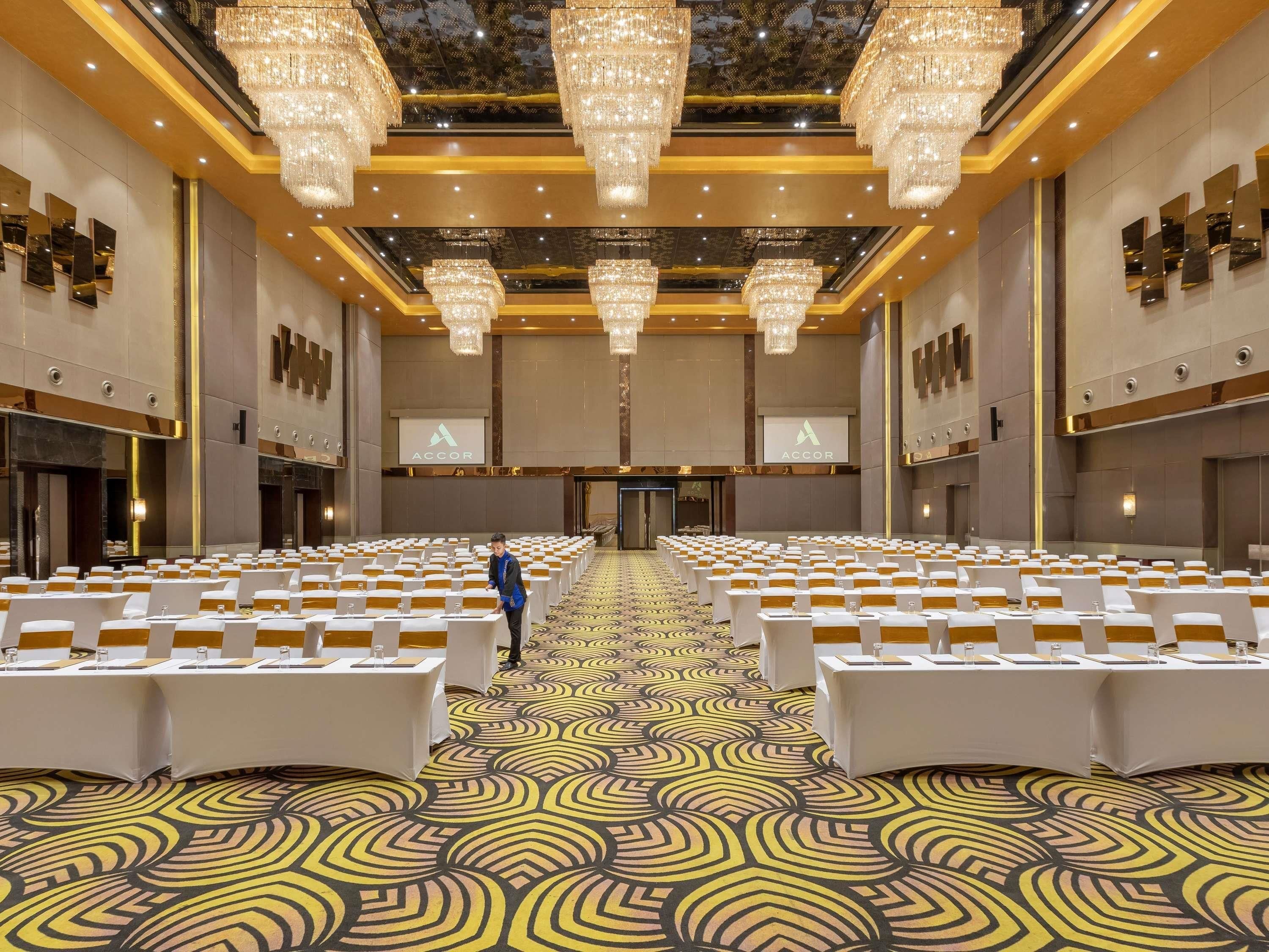 A large conference room with rows of tables, chandeliers, and a patterned carpet.