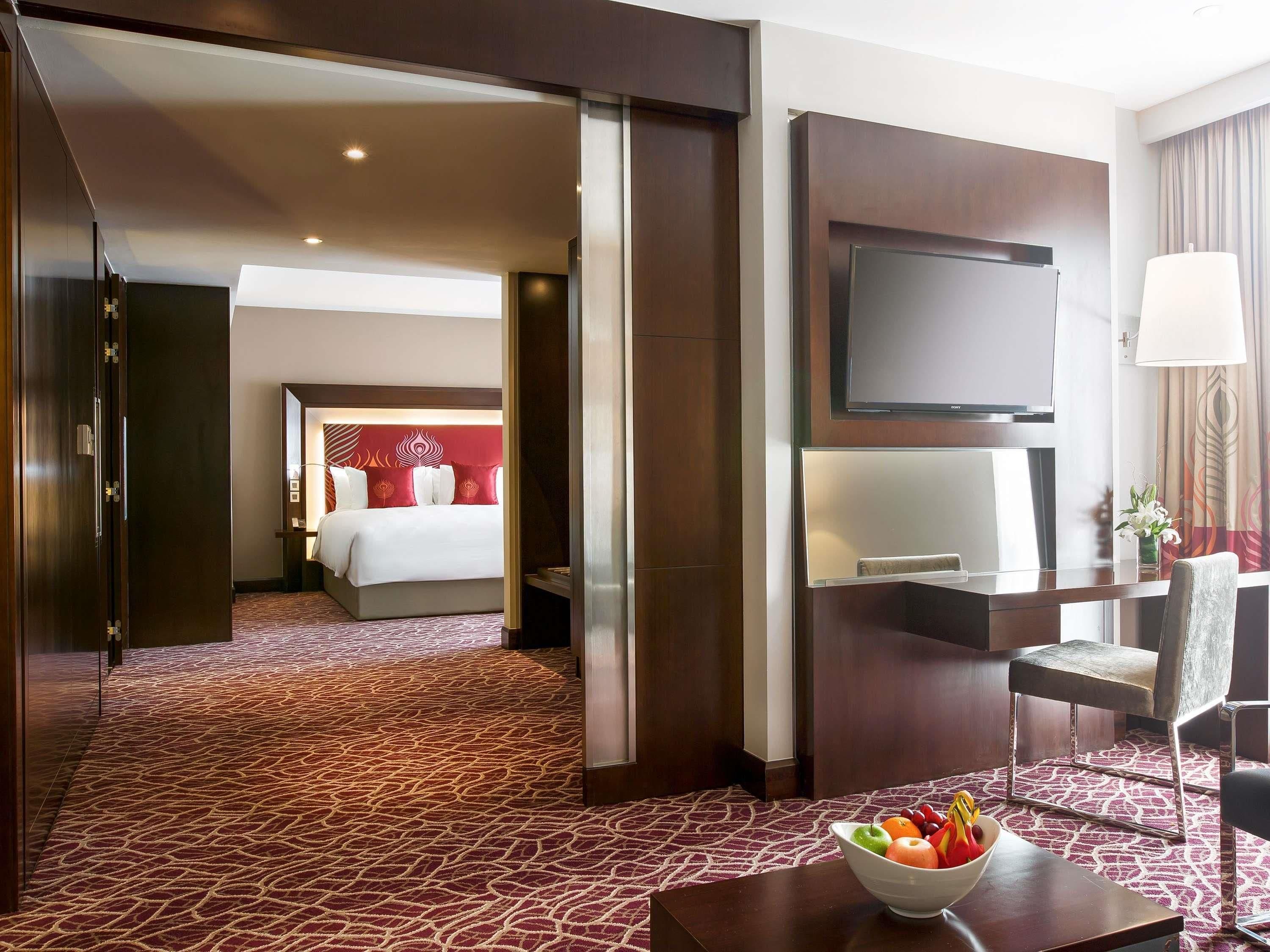 A hotel room with a bed, a desk, a chair, a TV, and a bowl of fruit on the desk.