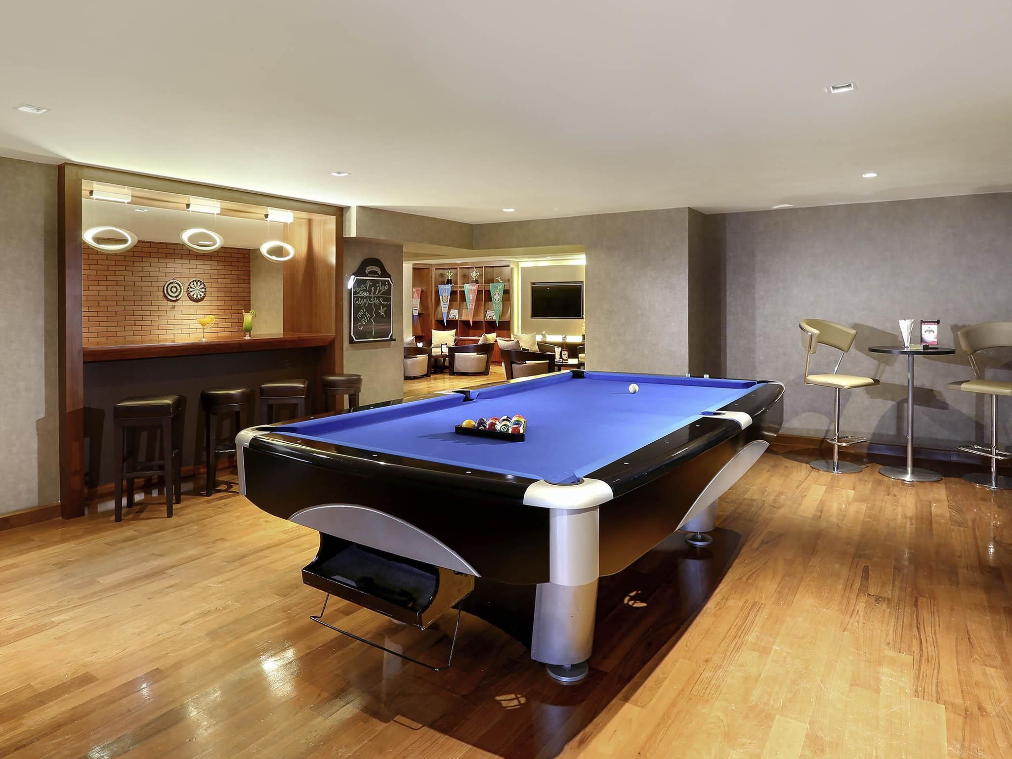Una mesa de billar en una sala con piso de madera, un área de bar con taburetes y un espacio de asientos con sillas.