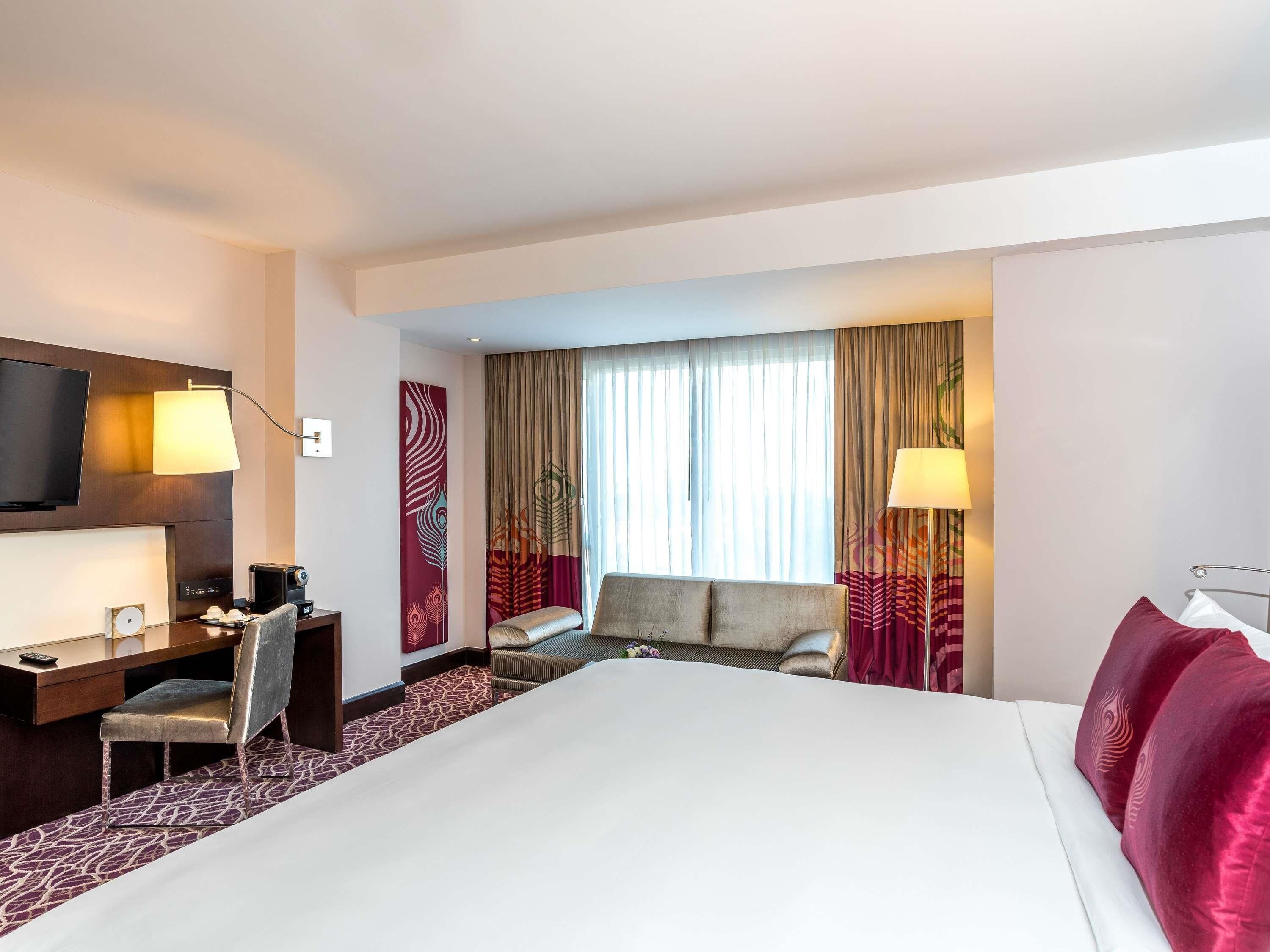 A hotel room with a large bed, a desk with a chair, a TV, and a window with curtains.