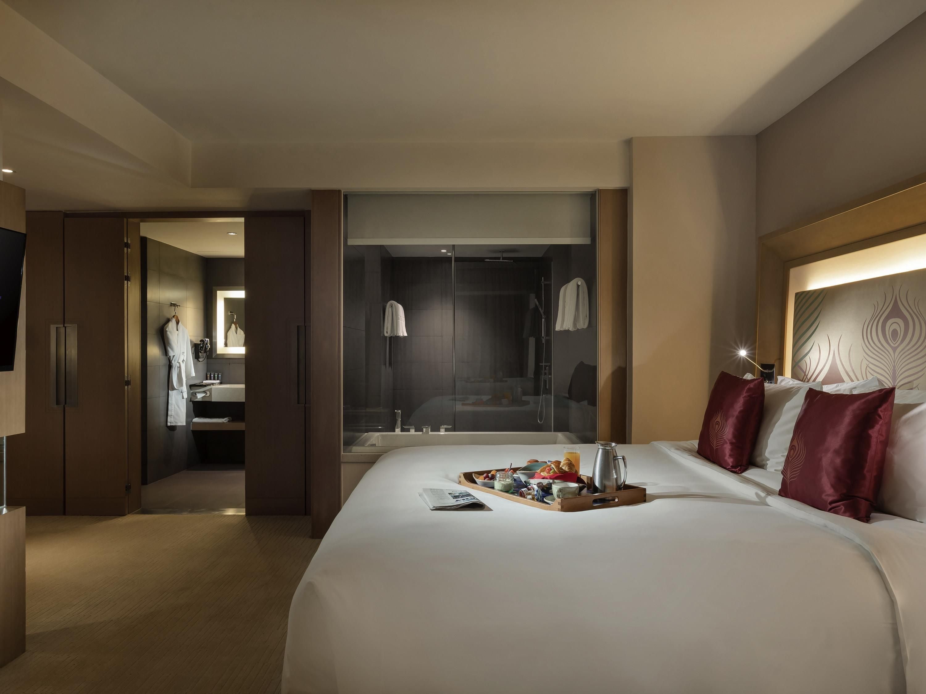 Une chambre d’hôtel avec un grand lit, une table de chevet sur laquelle se trouve un plateau avec des articles pour le petit-déjeuner, un espace douche et un miroir.