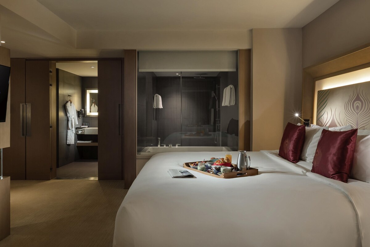 A hotel room with a large bed, a bedside table with a tray of breakfast items, a shower area, and a mirror.