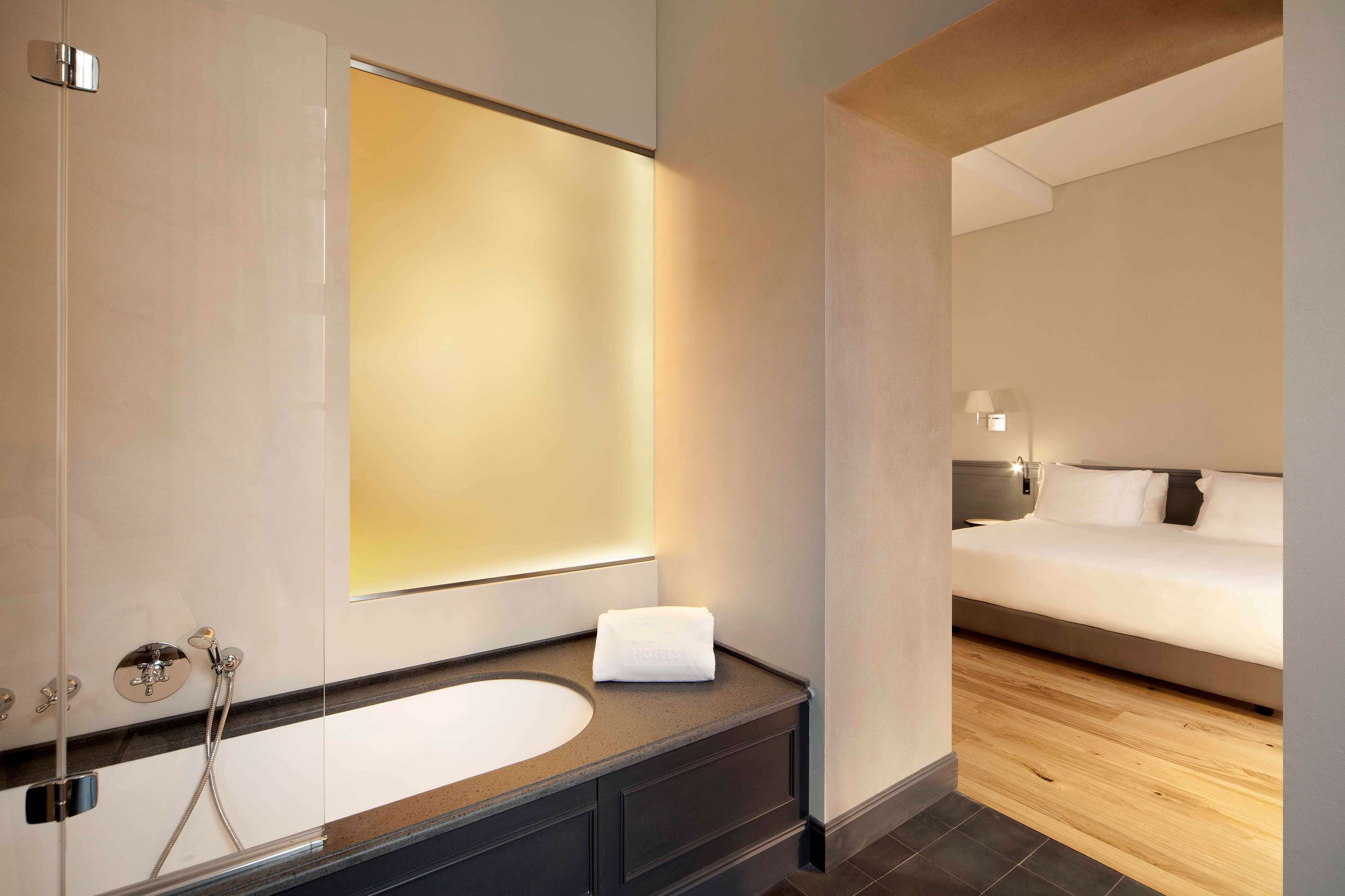 A modern bathroom with a large mirror, a bathtub, and a wooden floor.