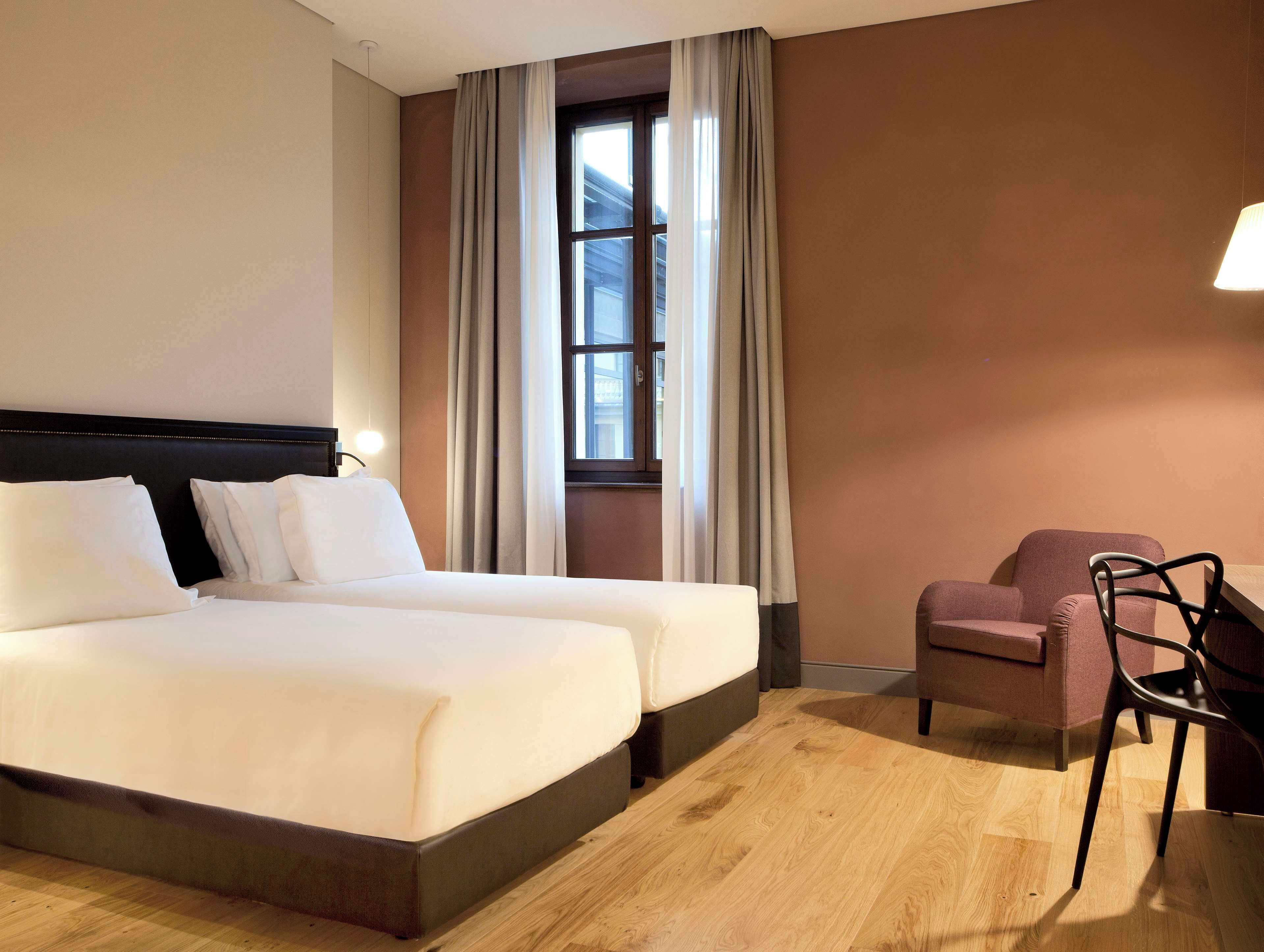 Habitación de hotel con cama doble, una silla y ventana con cortinas.