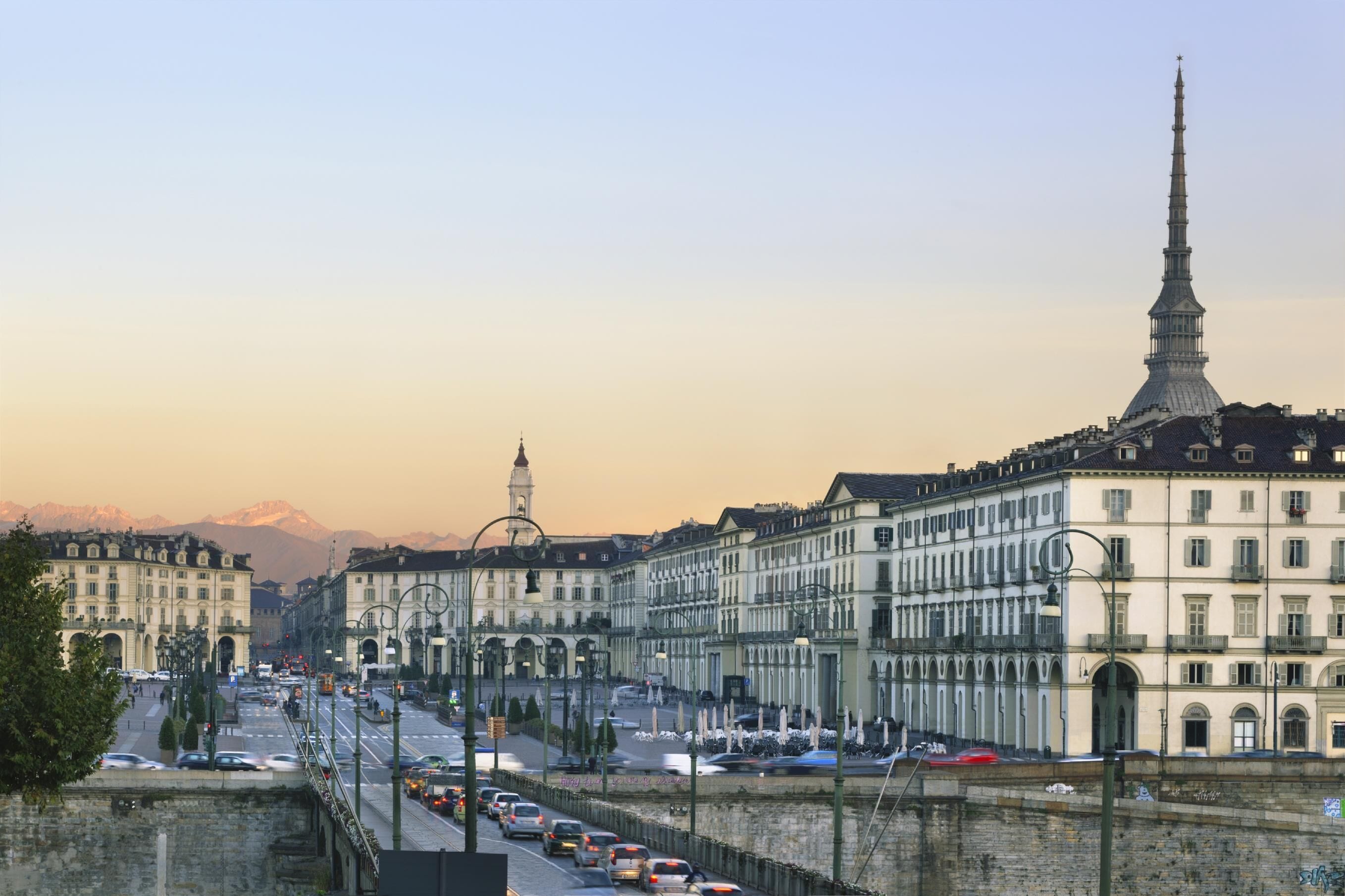Paesaggio urbano con edifici storici, una torre imponente e un ponte con auto.